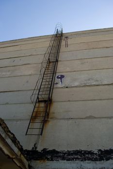 An old rusty staircase to the roof of the building. Abandoned industrial object.