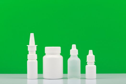 Set of medications for therapy, nose spray, pills and eye drops against green background with copy space. . Concept of health care and medications to treat cold-related diseases