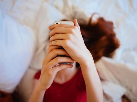 Woman with mobile phone writes message model red t-shirt bed. High quality photo