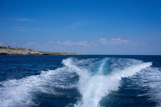White foam trail from the movement of the boat on a blue background. Travel by sea.