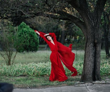 elegant woman in red dress posing near tree luxury summer. High quality photo