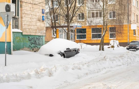 Lutsk, Ukraine - February 12,2020: Stuck car in snow and ice. City street after blizzard. Buried vehicle in snowdrift. Parking in winter after snowfall. Uncleaned road. Record-breaking amounts of snow