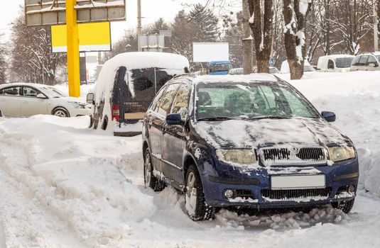 Lutsk, Ukraine - February 12,2020: Stuck car in snow and ice. City street after blizzard. Buried vehicle in snowdrift. Parking in winter after snowfall. Uncleaned road. Record-breaking amounts of snow