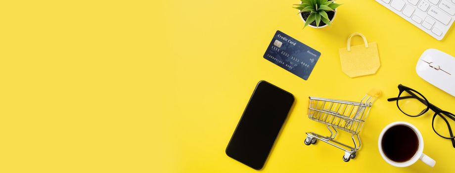 Top view of online shopping concept with credit card, smart phone and computer isolated on office yellow table background.