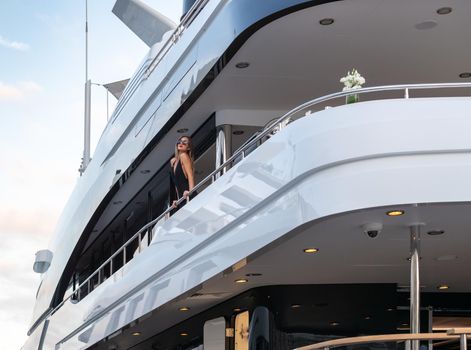 The elegant girl dressed in an evening dress of black color and sunglasses stands on the top deck of a huge yacht in anticipation, red lips, gorgeous lady, she does up hair, Monaco, Monte-Carlo