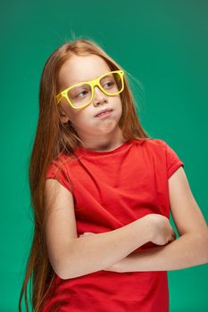 emotional red-haired girl in yellow glasses red t-shirt emotions studio green background. High quality photo
