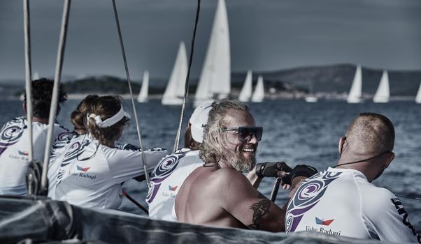 Sailboats compete in a sail regatta, the team turns off the boat, reflection of sails on water, multicolored spinnakers, number of boat is on aft boats, Croatia, Mediterranean Sea, 18 September 2019