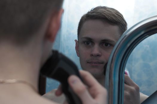 A young man of European appearance shaves an electric razor. Facial. High quality photo