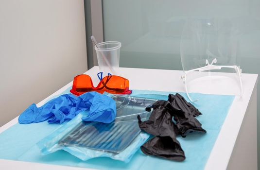 Sterile medical instruments in packaging and blue and black disposable gloves in a medical office. Surgical and dentistry equipment on the table.