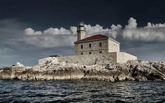 The island with a lighthouse at sunset, big white clouds are on background, reflection is on water, close up