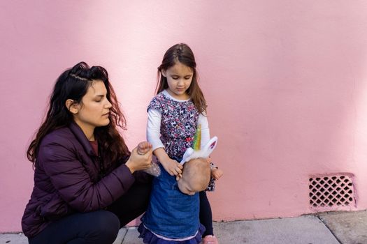 Beautiful view of woman and little girl holding cute baby with unicorn headband. Adorable baby girl holding her mother and older sister with pink wall as background. Happy family portraits