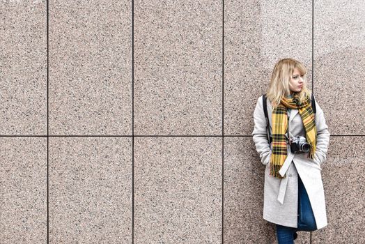 a blonde woman with a retro camera stands against the wall and looks away. free space. copy space