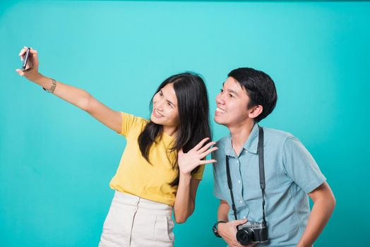 Portrait happy Asian young handsome man, beautiful woman couple smile standing wear shirt, taking selfie photo on a smartphone, studio shot on blue background with copy space