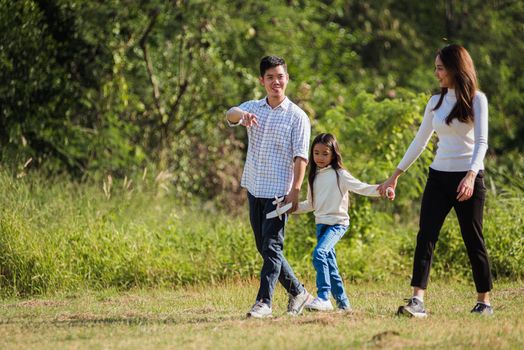 Happy Asian young family father, mother and child little girl having fun and enjoying outdoor walking down the road outside together in green nature park on a sunny summer day