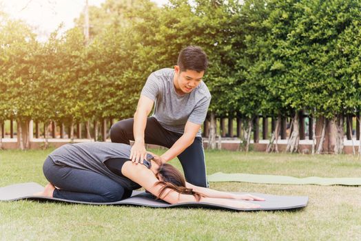 Asian man and woman training yoga outdoors in meditate pose sitting on green grass. Young couple practicing doing stretching in nature a field garden park together. Meditation health care concept