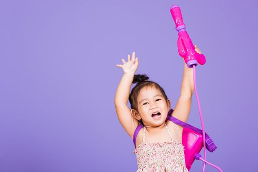 Happy Asian little girl holding plastic water gun, Thai child funny hold toy water pistol and smile, studio shot isolated on purple background, Thailand Songkran festival day national culture concept