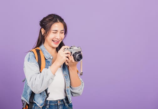 Attractive portrait happy Asian beautiful young woman smiling excited wear denims and bag holding vintage photo camera, female traveler female photographer, studio shot isolated on purple background