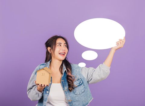 Happy Asian portrait beautiful cute young woman wear denim excited smiling hold house model and empty speech bubble sign, studio shot isolated on purple background, broker female real estate insurance