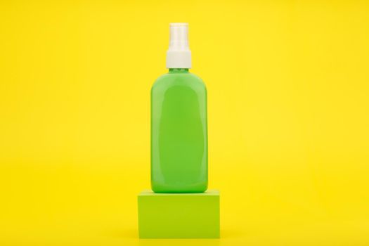 Still life with spray for sun protection with sunscreen in green tube on podium against yellow background with copy space. Concept of safe tan and beauty products with spf factor 
