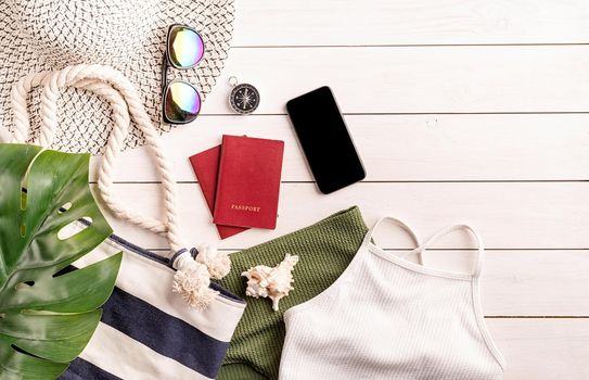 Travel and vacation concept. Flat lay travelling objects with swimsuit, smartphone, passports, sunglasses and compass on white wooden background