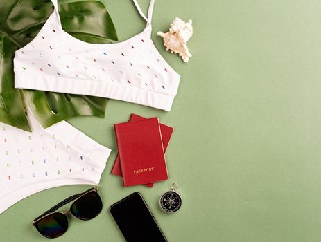 Travel and adventure. Flat lay travelling objects with monstera leaf, swimsuit, passports, sunglasses and compass on green background with copy space