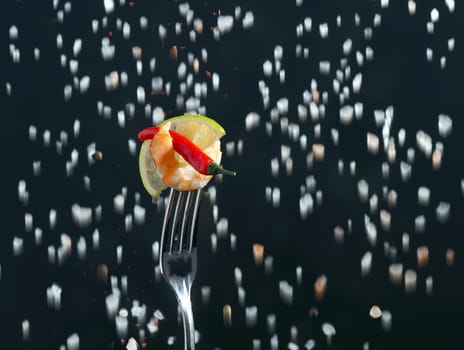 Shrimp on a fork boiled with a slice of lemon on a black background and large salt in the background. High quality photo