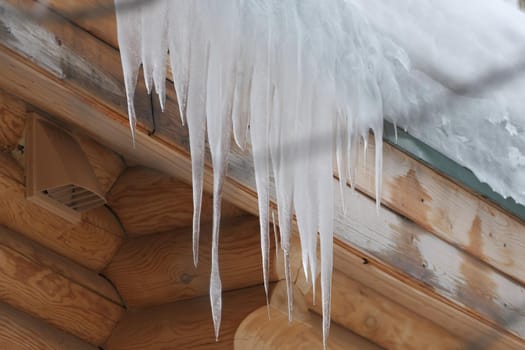 Large icicles hang from the roof of a log house. Winter frost and spring drops. High quality photo