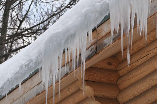 Large icicles hang from the roof of a log house. Winter frost and spring drops. High quality photo