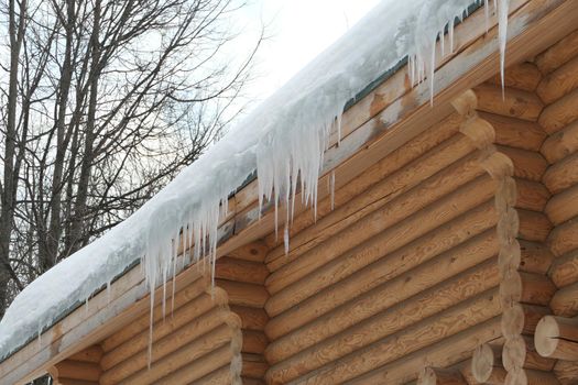 Large icicles hang from the roof of a log house. Winter frost and spring drops. High quality photo