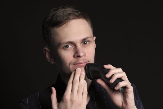 Shave safely. A young man or man of European appearance shaves his face with an electric razor. High quality photo