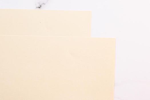 Beige A4 papers on white marble background as office stationery flatlay, luxury branding flat lay and brand identity design for mockups