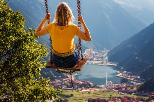 Young female on a swing with the view of the mountain lake Uzungol, Trabzon, Turkey.