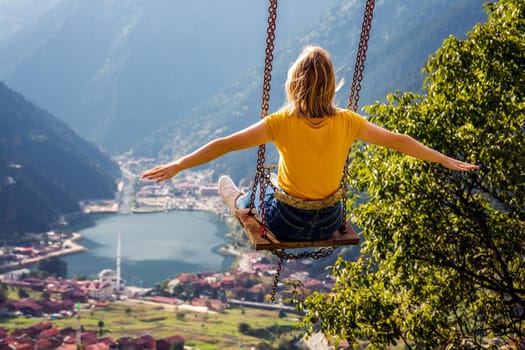 Young female on a swing with the view of the mountain lake Uzungol, Trabzon, Turkey.