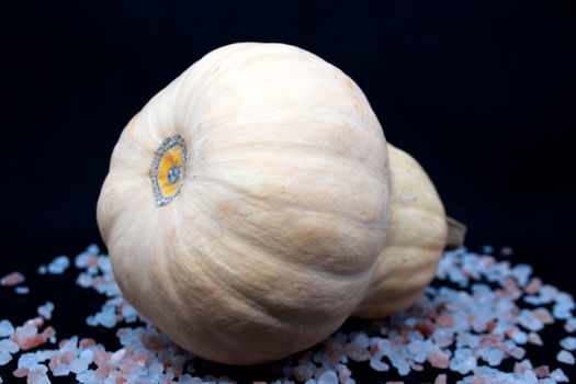 Pumpkin lies with pink sea salt on a black background.