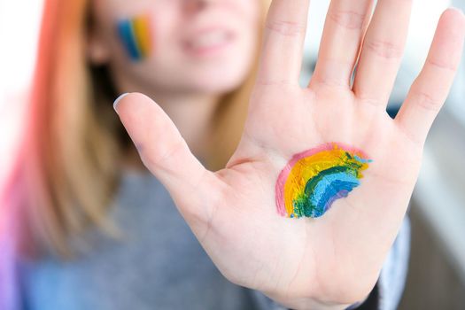 Rainbow LGBTQ flag painted on hand and cheek. Support for lgbt community. Honour of pride month. Connecting people, touching hands. Multi colored hands art creativity, discrimination. Selective focus