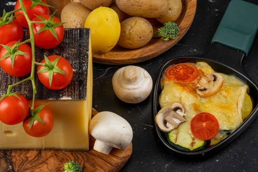 Delicious traditional Swiss melted raclette cheese on chopped boiled potatoes with vegetables.