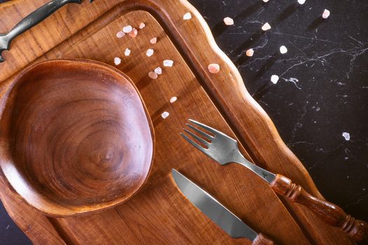 Empty wooden plate on a wooden table with cutlery and salt particles. Top view.