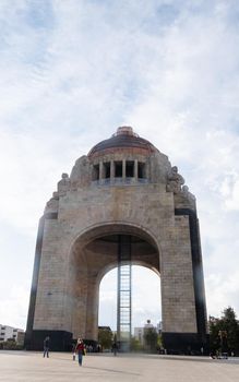 Mexico City, Mexico - January 13, 2021: Monument to the Revolution with slightly cloudy sky as background. Majestic triumphal arch in Mexico City with people passing by. Mexican landmarks