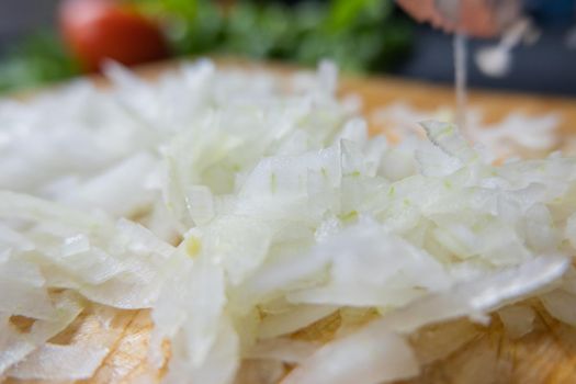 Close-up of chopped onions on wooden cutting board with blurry coriander as background. Fresh vegetables and herbs cut into pieces above wood surface. Traditional sauce preparation