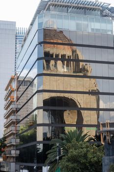 Reflection of the Monument to the Revolution on the windows of tall and modern building. Mirror-like building reflecting triumphal arch from Mexico City. Mexican landmarks