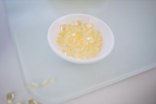 Close-up of small bowl of vitamin C pills on transparent cutting board. Transparent capsules in porcelain bowl above white surface. Vitamin C nutrition