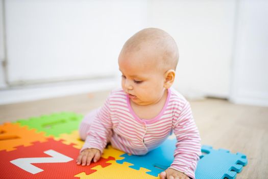 Adorable baby lying face down on colorful children mat with letters. Portrait of distracted-looking baby playing on the floor. Happy babies having fun