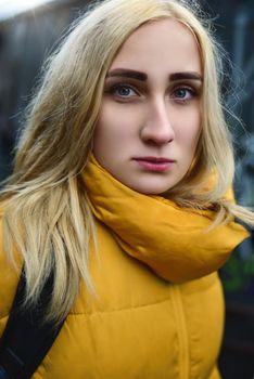 Close up portrait of blonde hipster teen girl making selfie, She is wearing yellow jacket and backpack, walking outdoors throught underground passage and making selfie
