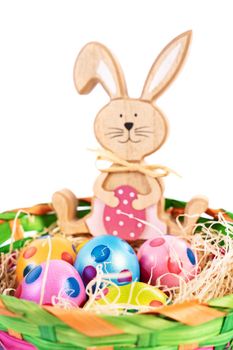 Close up of colourful Easter eggs with polka dots in a basket together with a toy Easter bunny, isolated on white background. Fun and colourful Easter celebration concept.