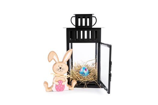 Wooden Easter bunny with a colourful Easter egg in a nest within a decorative lantern, isolated on white background. Fun and colourful Easter celebration concept. Easter decoration concept.