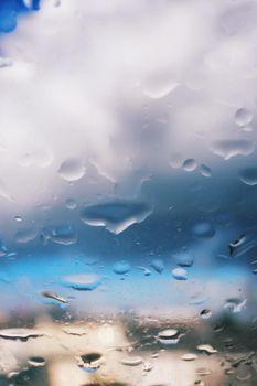 Selective focus of rain drops on a glass window surface with beautiful blurry sky and clouds in the background. Dramatic background concept. Light after the storm.