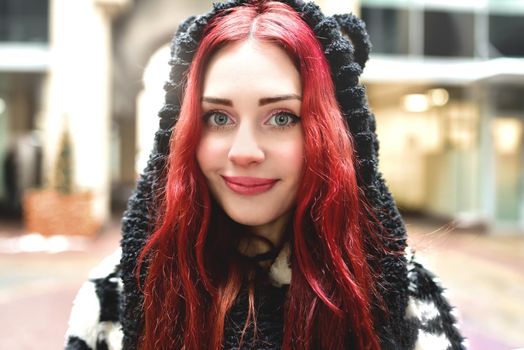 Close portrait of a smiling teen girl with red hair in warm clothes standing outside and looks into the camera