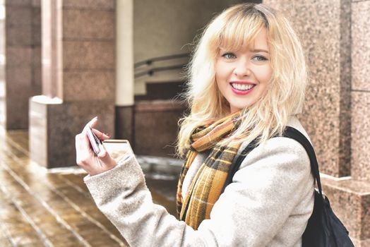 beautiful smiling caucasian blonde girl straightening her makeup , walking in the city