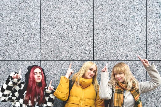 Cheerful girls at the street, show a big sale, or nice offer. Advertise concept. People, travel and tourism - women on city street show with their fingers something over gray wall background