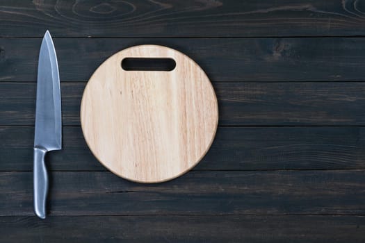 Close up kitchen knife and wooden round empty cutting board on a wooden table